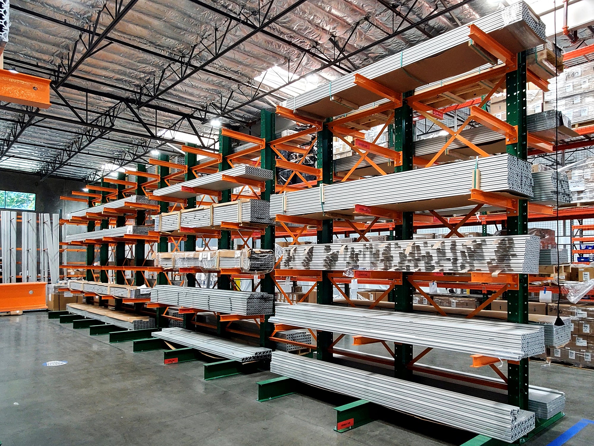 Warehouse filled with green and orange shelving with metal organized on the shelving